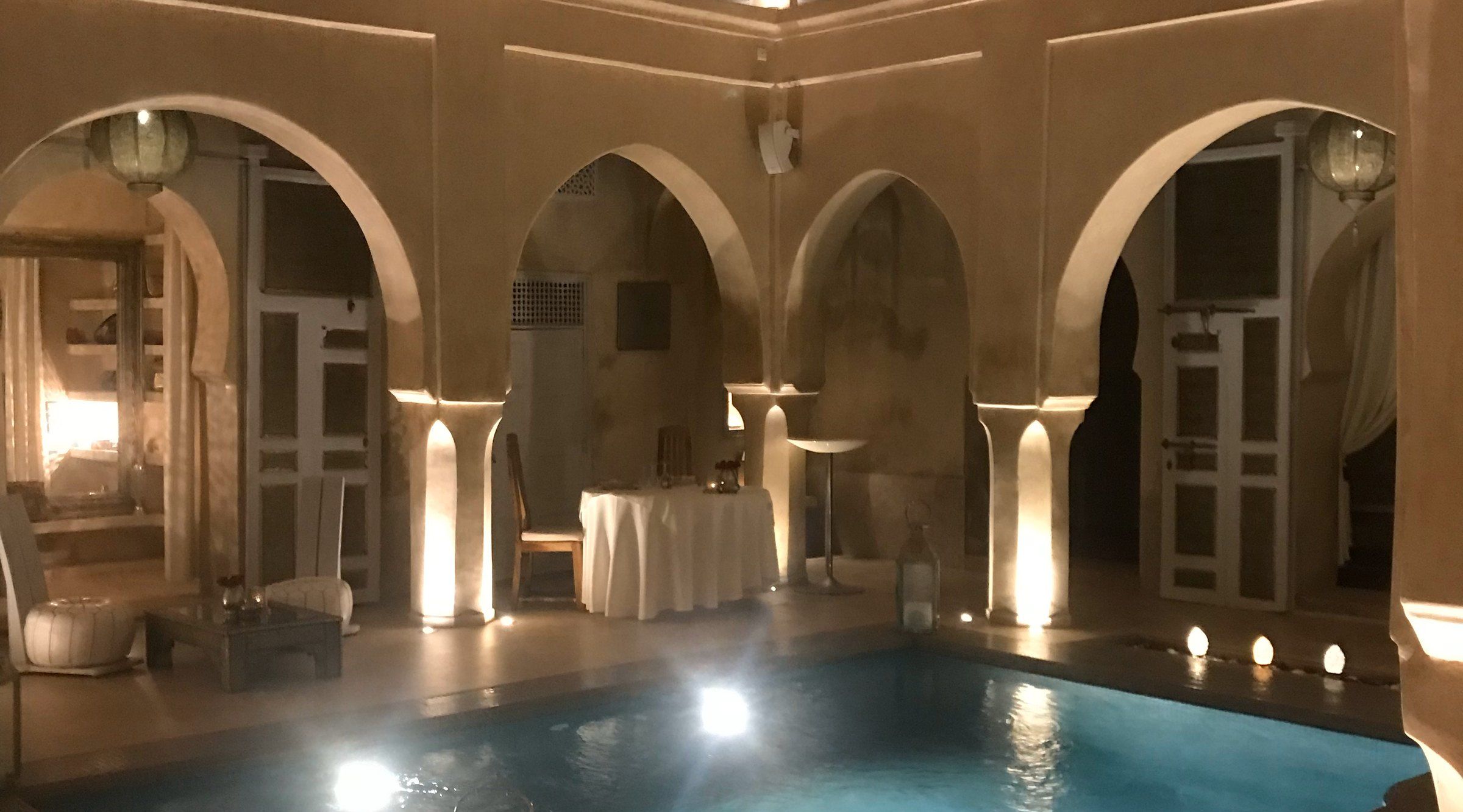 Arched courtyard of a riad in Marrakech at night, with a small lit pool